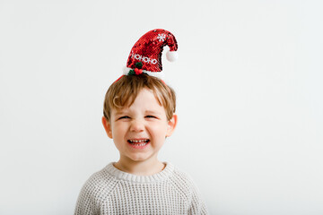 Funny little boy with Christmas headband laughing on light wall background