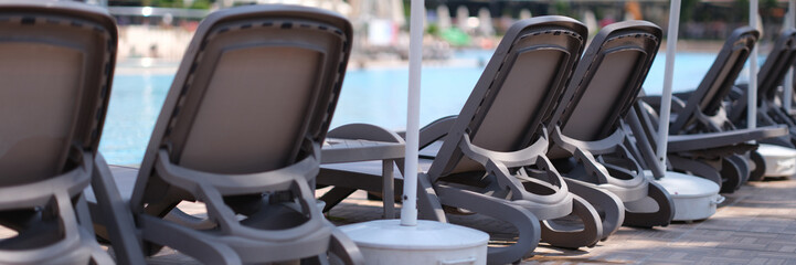 Many empty sun loungers and parasols standing near swimming pool