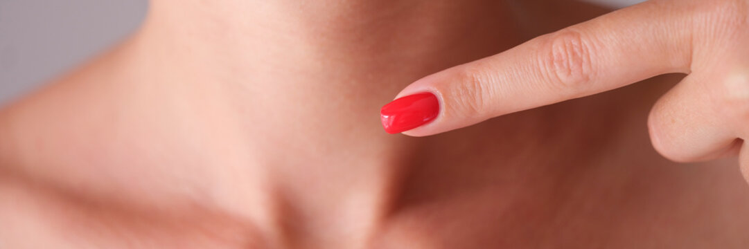 Woman with red manicure pointing finger at neck area with thyroid gland closeup