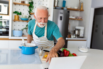 Happy senior man having fun cooking at home - Elderly person preparing healthy lunch in modern...