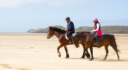 Father and daughter enjoying horse riding together on beach in Anglesey Wales.Horses enjoying the freedom to move on beach people enjoying living the dream, riding together at the seaside.