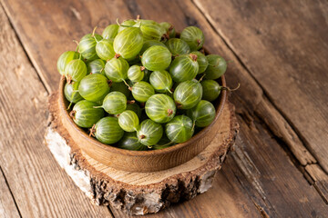 Green gooseberries in a wooden bowl. Harvest berries on a wooden table. Gooseberry summer vitamin food.