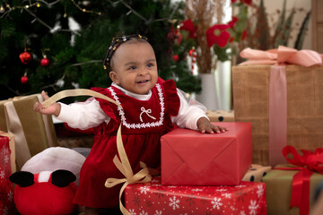 Fototapeta na wymiar Adorable African baby girl with African braid hairstyle among many wrapped Christmas gifts, happy new year and merry Christmas, winter holidays and people concept