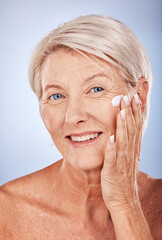 Portrait, skincare and senior woman with face cream for moisturizing on blue studio background. Beauty, smile or elderly female model apply facial creme, cosmetics product or lotion for healthy skin