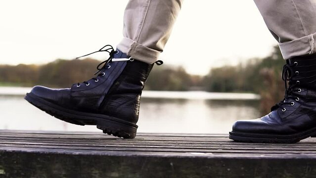 Close up view of black leather boots walking by a lake in nature outdoor park