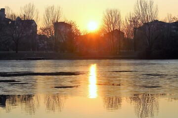 evocative image of sunset over the water with silhouette of houses and trees in the background
