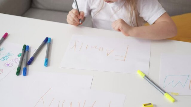 Kids education. Art creativity. Foreign lesson. Unrecognizable girl drawing word family with colorful markers on paper sitting desk light room interior.