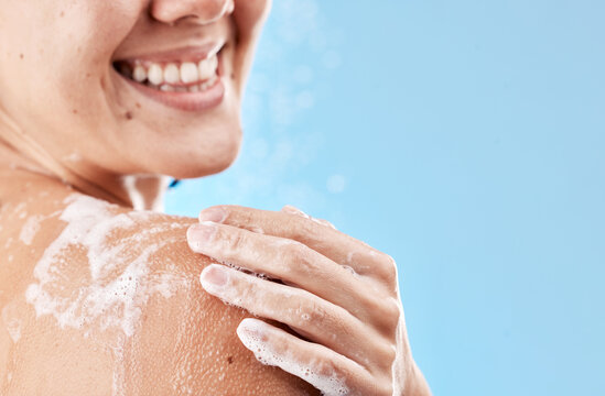 Shower, soap and smile of a woman grooming body for health, skincare and wellness against a blue mockup studio background. Water, cleaning and hand of a model with foam on shoulder and mock up space