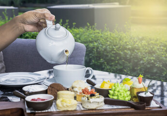 Hand holding Chinese tea pot pouring hot tea serving with sets of bakery in garden, Food-Bakery concept