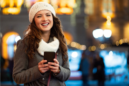 Portrait of young smiling beautiful woman using smartphone on the street at winter