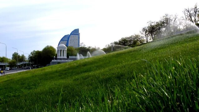 Volgograd, Russia - May 07, 2022: A lawn sprinkler sprays water on the green grass on the slope of the Central embankment in Volgograd
