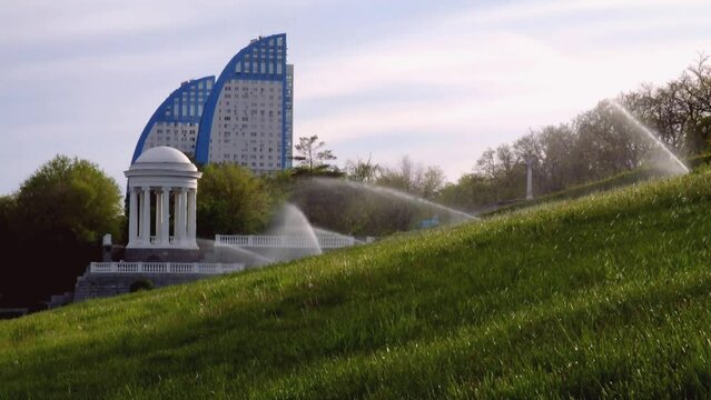 Volgograd, Russia - May 07, 2022: A lawn sprinkler sprays water on the green grass on the slope of the Central embankment in Volgograd