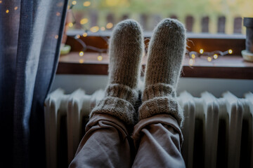 Women's legs feet in woolen socks on a heating battery