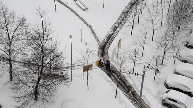 Worker removes snow with a snow blower in yard of city (top view)