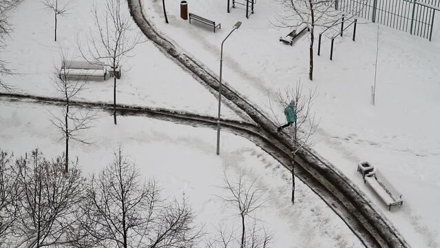 A schoolgirl walks along a road cleared of snow and along a snow-covered road in the courtyard of the city (top view)