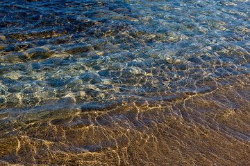 Aquamarine and yellow waves above the texture rivulets of sand on the shoreline of the Mediterranean coast in Israel.