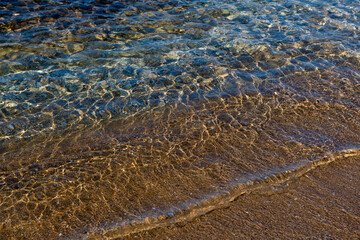 Aquamarine and yellow waves above the texture rivulets of sand on the shoreline of the Mediterranean coast in Israel.