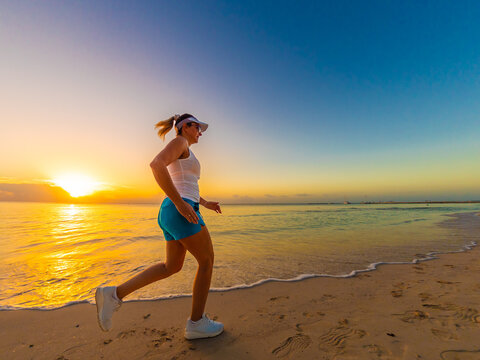 Woman running on sunny, tropical beach at daybreak
