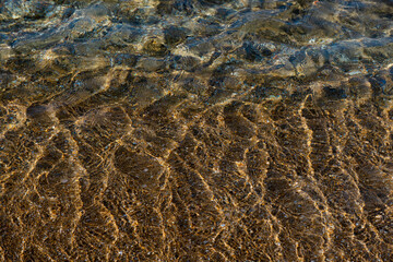 Aquamarine and yellow waves above the texture rivulets of sand on the shoreline of the Mediterranean coast in Israel.