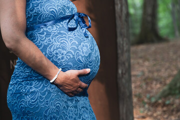 Mom in blue dress touches her pregnant belly.