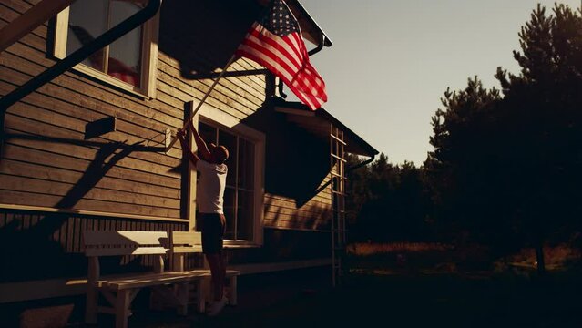 Proud American Homeowner Flying the United States of America National Flag on His Residential Area Home. Adult Man Fixing the Flag on His House Wall. Perfect Summer Day to Celebrate Patriotism.