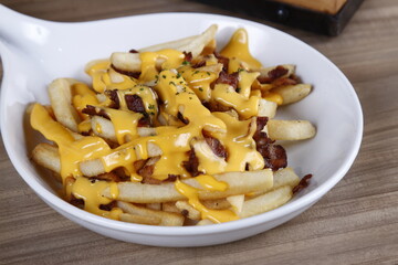 Cheesy French fries with bacon bits on a white plate