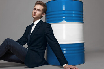 A manager in a suit sits near a barrel of fuel on a gray background.