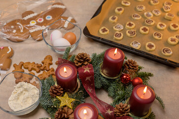 Lit advent wreath with Christmas decor and raw cookies sitting on a baking tray 