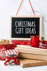 Christmas gift ideas. Xmas holiday gift for everyone. Text Christmas gift ideas on black board and Red and brown zero waste cup, shopper bag, socks, notepad, sweets, cookies on table