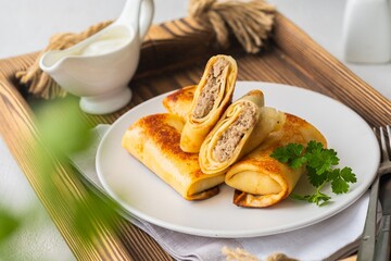 Thin pancakes stuffed with boiled minced meat with fried onions on a white plate on a light concrete background. Pancake recipes.