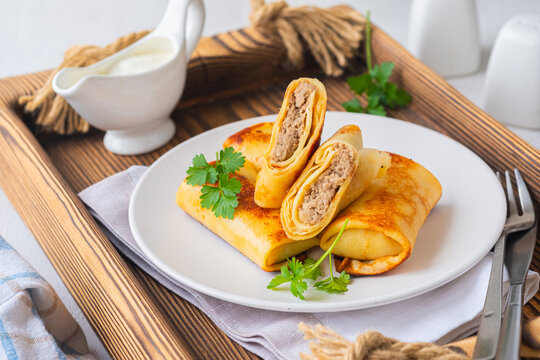 Thin pancakes stuffed with boiled minced meat with fried onions on a white plate on a light concrete background. Pancake recipes.