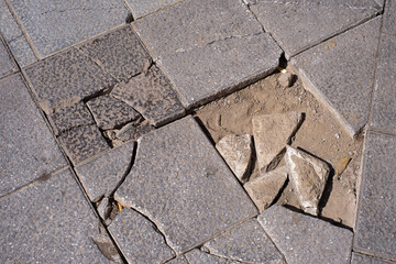 Close-up of the textures of the broken tiles of an avenue. Hollow of broken tiles. Broken gray...