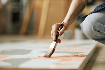 Obraz premium Selective focus on hand of young creative woman with paintbrush creating abstract painting on canvas while squatting on the floor