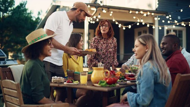 Portrait of a Family and Friends Celebrating Outside in a Backyard at Home. Diverse Group of Children, Adults and Old People Gathered at a Table, Talking, Sharing Experiences and Having Fun.