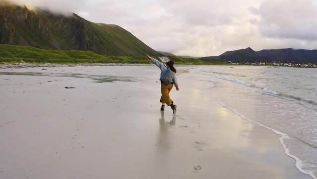 heerful girl runs with her hands up in joy. Village on Andoya Blake Island. Vesteralen Archipelago, Norway