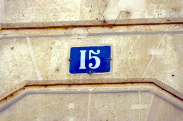 Numéro 15. Plaque de numéro de rue sur façade de pierre.