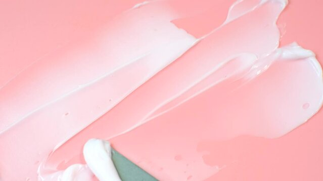 Smear of a moisturizing face cream using spatula on pink background.