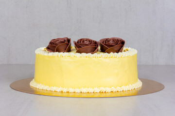yellow cream cake with brown roses on a gray background close-up