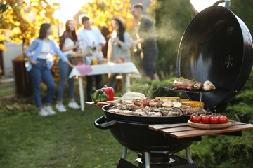 Group of friends having party outdoors. Focus on barbecue grill with food. Space for text - obrazy, fototapety, plakaty