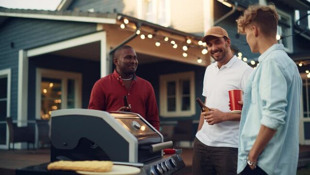 Three Happy Young Adult Men Gathered Around a Fire Grill, Chatting and Telling Funny Stories while Preparing Barbecue Beef Steak. Friends Spending Time Outdoors, Talking, Relaxing, Drinking Beers.