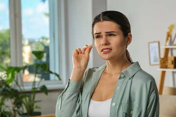 Young woman cleaning ear with cotton swab in room