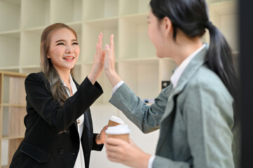Two Asian businesswomen giving high five to each other, celebrating their project success