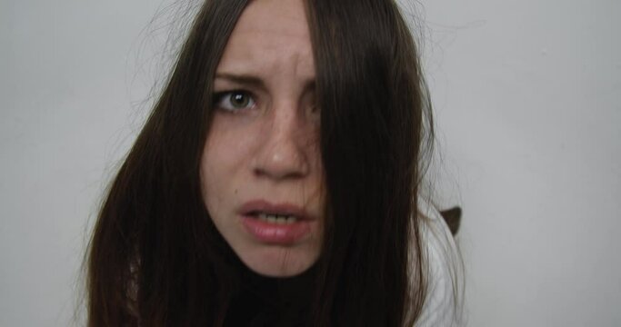 Extreme close up  of teenager girl with face covered with  long red hair, dressed in straitjacket, barefoot, tied with straps, sits in the corner of Ward in mental hospital. Attack of schizophrenia, 