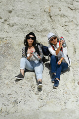 Two happy retired women travelers sitting front of rock cliff walls. People, friendship and active retirement healthy lifestyle concept