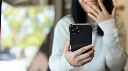 Amazed and cheerful young Asian woman using her smartphone while relaxing in the coffee shop.