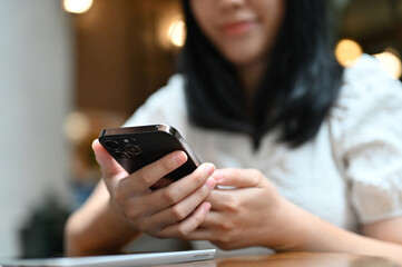 Charming young Asian female using her smartphone while relaxing in the cafe. texting, messaging