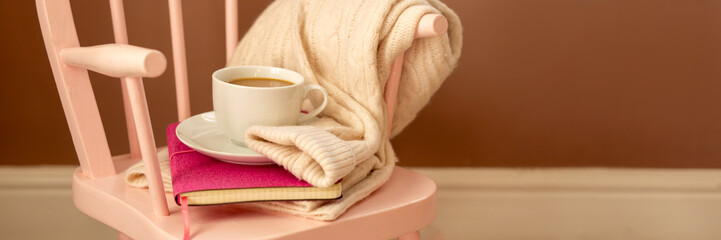 A pink baby rocking chair against the wall with delicious cocoa, a sweater and a book. Banner