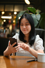 Beautiful Asian woman using her mobile phone while relaxes sitting at the coffee shop.