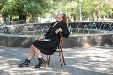 girl model posing sitting. beautiful young woman on a bench with a book. girl in a black dress.