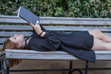 girl reads a book in the park outdoors. beautiful young woman on a bench with a book. girl in a black dress.